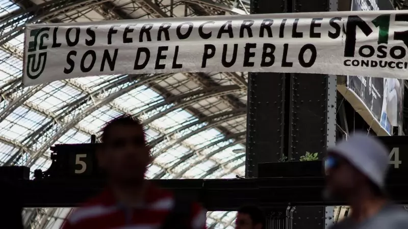 Los viajeros caminan mientras una pancarta que dice 'Los trenes pertenecen al pueblo' cuelga en la estación de tren de Retiro, durante un paro nacional de