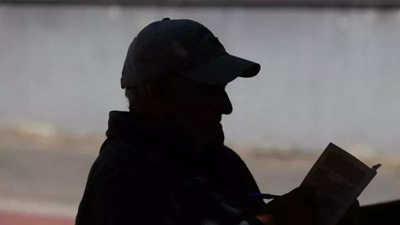 Un anciano lee un libro en un banco de un parque en Madrid.