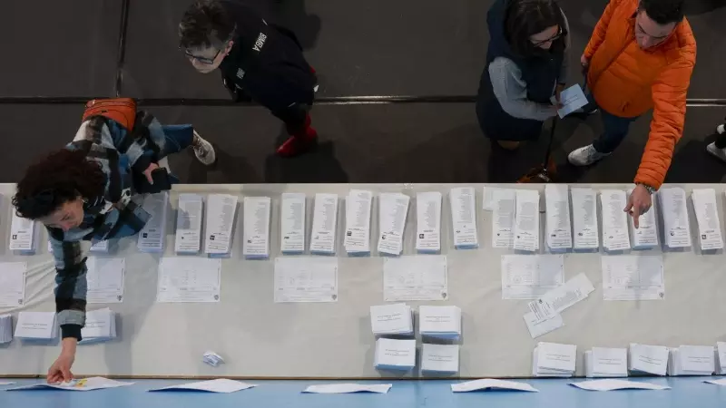 Varias personas escogen papeletas para ejercer su derecho al voto en el pabellón polideportivo Ames en A Coruña durante la jornada electoral en Galicia, este domingo.