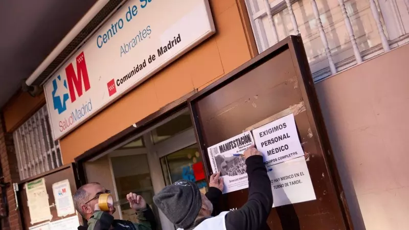 Dos hombres pegan carteles en la puerta del Centro de Salud de Abrantes, a 16 de febrero de 2023, en Madrid.