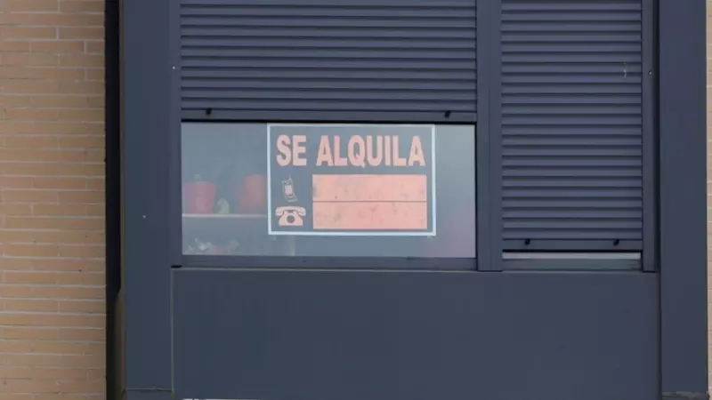 La fachada de un edificio donde se ve un cartel de 'Se Alquila' bajo la persiana de uno de los pisos.