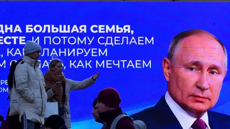 Un grupo de transeúntes pasan cerca de una pantalla digital que muestra una imagen Vladimir Putin, en San Petersburgo, a 14 de marzo de 2024.