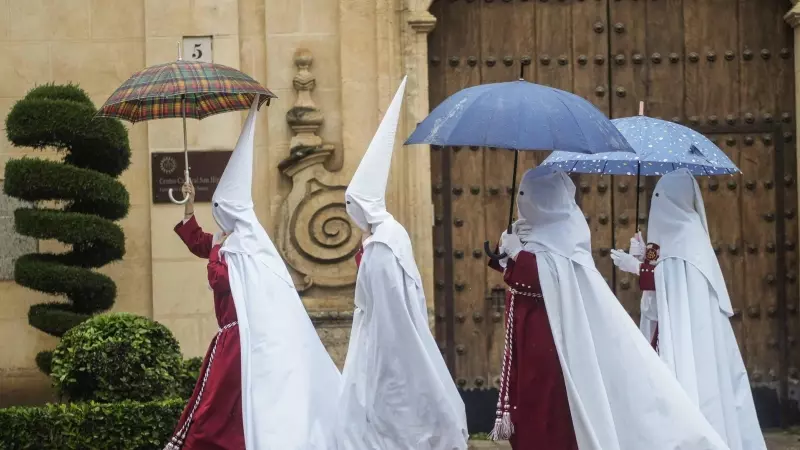 Unos nazarenos de la Hermandad de La Sentencia se protegen de la lluvia con paraguas en Córdoba este lunes 25 de marzo de 2024.