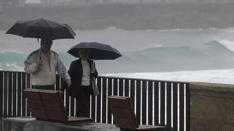 Dos personas caminan con un paraguas al lado de la playa del Orzán (A Coruña), en una foto de archivo.