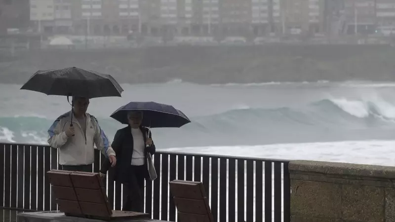 Dos personas caminan con un paraguas al lado de la playa del Orzán (A Coruña), en una foto de archivo.