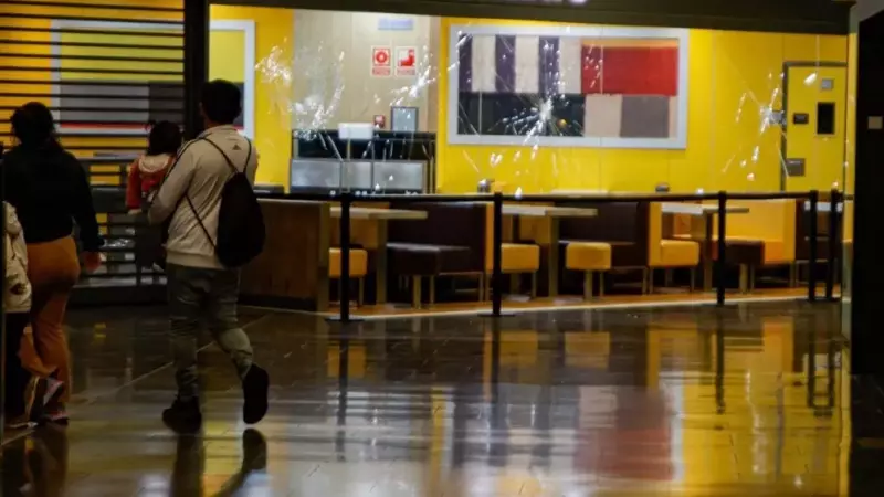 Dues persones passen davant de l'aparador del McDonald's amb els vidres trencats al centre comercial Màgic Badalona