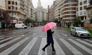 Un hombre protegido con paraguas en la plaza del Ayuntamiento de Valencia prácticamente vacía durante el decimoséptimo día del estado de alarma decretado por el Gobierno. EFE/Kai Försterling