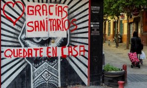 Una mujer con un carro de la compra pasa junto a un comercio cerrado con una pintada de agradecimiento a los sanitarios en una céntrica calle de Sevilla, hoy miércoles en la séptima semana de confinamiento decretado en el Estado de Alarma debido a la cris