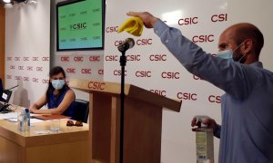 Un asistente desinfecta el micrófono mientras la investigadora Mar Valés (izquierda) da una rueda de prensa, junto al equipo de investigadores, en la sede del Consejo Superior de Investigaciones Científicas (CSIC) en Madrid. EFE/J.J. Guillén