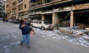 Una mujer lleva a un niño mientras pasa por las tiendas dañadas tras la explosión del martes en Beirut, Líbano