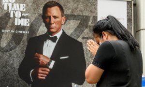 Una mujer reza frente a un cartel publicitario que presenta a Daniel Craig en la nueva película de James Bond.- AFP