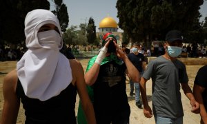 El gesto de palestinos enmascarados cuando la Cúpula de la Roca se ve en el fondo luego de los enfrentamientos con la policía israelí en el complejo que alberga la Mezquita de al-Aqsa, conocida por los musulmanes como el Noble Santuario y por los judíos c