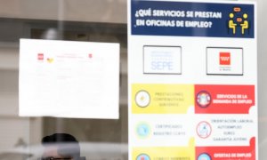 Un hombre con mascarilla tras el cristal de la puerta de una oficina de empleo, SEPE.