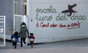 Una madre acompaña a sus hijos a la escuela Turó del Drac de Canet de Mar. Una pintada reclama la enseñanza en catalán en la fachada del centro. — Jordi Pujolar