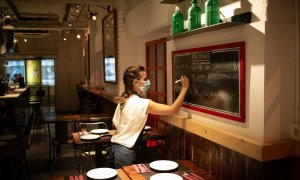 Una camarera apunta platos en una pizarra en el interior de un bar en una calle céntrica de Barcelona
