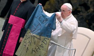 12/04/2022 - El papa Francisco muestra una bandera de Ucrania que fue enviada desde la localidad de Bucha durante la audiencia semanal en el Salón de Pablo VI en el Vaticano.