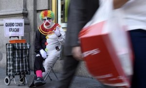 Rayito, un mendigo disfrazado de payaso, saluda sentado junto a un cartel que dice "Quiero comer, gracias" en la calle Gran Vía, en el centro de Madrid, el 28 de octubre de 2014.