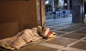 Un hombre sin techo duerme en la acera, junto a una cafetería. EFE