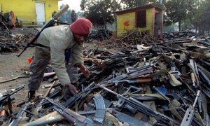 A Zairean soldiers inspects piles of weapons confiscated to Rwandan government troops after they fled the border city of Gicenyi, Rwanda July 18, 1994. REUTERS/Corinne Dufka/File Photo