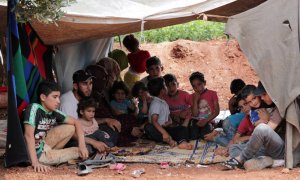 Un agricultor sirio desplazado sostiene a su hija mientras se sienta con otros miembros de la familia en un olivar en la ciudad de Atmeh, provincia siria de Idlib. REUTERS / Khalil Ashawi