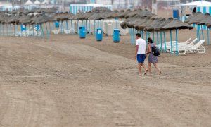Una pareja pasea por la playa de la Malvarrosa en la que la afluencia de gente ha descendido notablemente debido en gran medida al descenso de temperaturas, a los chubascos y al cielo nublado. /EFE