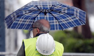 Un trabajador de la construcción se protege de la lluvia con un paraguas en Valencia. EFE/Kai Försterling