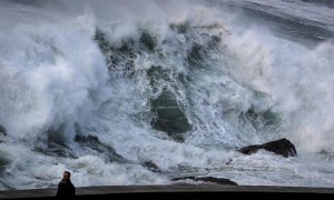 Un hombre pasea este domingo ajeno a una gran ola a punto de romper en el Paseo Nuevo de San Sebastián. EFE