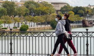 Dos jovenes con mascarillas paseando andando por el puente de Triana. /EUROPA PRESS/Archivo