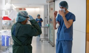 Un professional sanitari ajuda una companya a protegir-se abans d'atendre un pacient amb covid-19, en un dels blocs quirúrgics de l'Hospital Clínic de Barcelona habilitat com a UCI en la pandèmia de coronavirus. ACN/ Francisco Àvia / Hospital Clínic