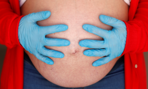 Una embarazada de 9 meses usa guantes mientras se toca el vientre durante el confinamiento por coronavirus. REUTERS / Jon Nazca