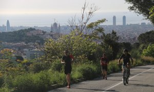 Pla general d'un ciclista i dos corredors pujant pel carrer Manuel Arnús, just abans d'arribar a la carretera de les Aigües, al Parc de Collserola de Barcelona. Imatge del 2 de maig de 2020. (Horitzontal)