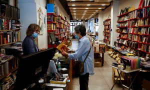 04/05/2020.- El librero Eric del Arco (i), de la histórica librería Documenta de Barcelona, atiende a una clienta. / EFE - QUIQUE GARCÍA