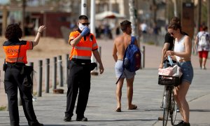 Agentes Civicos indican a una joven que se coloque la mascarilla protectora, este sábado en el paseo marítimo de la Barceloneta en Barcelona. EFE/Toni Albir