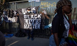 Un hombre (L) con una máscara facial vende banderas y otros accesorios con el eslogan 'Black Lives Matter'
