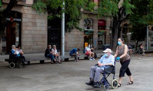 Una mujer empuja la silla de un anciano en el centro de Barcelona.  - EFE