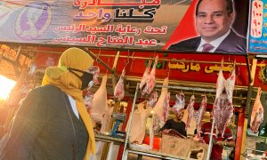 Una mujer con mascarilla camina frente a una carnicería con una pancarta del presidente egipcio, Abdel Fattah al-Sisi, en el mercado de Al Ataba, en El Cairo. - REUTERS