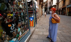 Una mujer con mascarilla, delante de una tienda de souvenirs turísticos en Barcelona. REUTERS