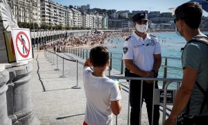 Un agente de la Policía Municipal impide el acceso este miércoles a la playa de La Concha de San Sebastián, coincidiendo con la pleamar, para evitar un exceso de aforo. EFE/Javier Etxezarreta