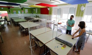 Xavi Leal y Carolina Ramos, director y jefa de estudios, respectivamente, del CEIP Jaume I de Catarroja, colocan los parabanes, realizados con unos percheros y una lámina de plástico transparente, para prepararse para la vuelta a las aulas en la Comunita