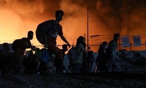 Un grupo de refugiados carga con sus pertencias mientras huye del incendio que ha arrasado el masificado campo de Moria, en Lesbos, Grecia, días después de que se detectara el primer positivo por covid.- REUTERS.