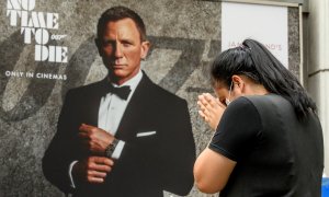 Una mujer reza frente a un cartel publicitario que presenta a Daniel Craig en la nueva película de James Bond.- AFP