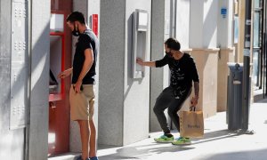 Dos jóvenes operan en sendos cajeros automáticos de dos entidades bancarias, en la localidad malagueña de Ronda. REUTERS/Jon Nazca