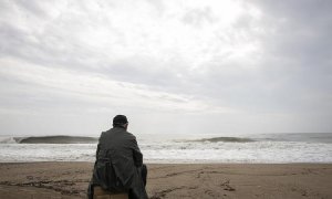 Un hombre mira al  mar en una playa mientras está nublado.