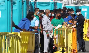 Varios migrantes esperan en el muelle de Arguineguín (Gran Canaria) a que les tomen las huellas dactilares y la filiación.