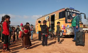 Un grupo de niños participa en una actividad al aire libre junto a un autobús especial utilizado como aula improvisada en el campamento de Haranbush para sirios desplazados en el norte de la provincia de Idlib, en el noroeste de Siria. Fotografía del 7 de