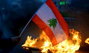Un manifestante antigubernamental lleva una bandera libanesa mientras otros manifestantes queman neumáticos para bloquear la carretera principal durante una protesta contra los cortes de energía, el alto costo de vida y el bajo poder adquisitivo de la lib