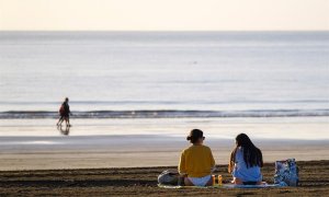 Dos jóvenes charlan en la playa de Maspalomas, en el sur de Gran Canaria, este martes a primera hora de la mañana, en un día con el cielo totalmente despejado.