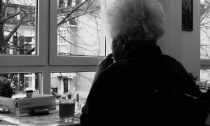 Una persona mayor mira por la ventana de su casa.