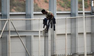 Un migrante encaramado a la valla fronteriza que separa Ceuta de Marruecos, este martes 13 de abril,