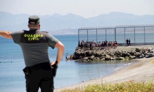 Un agente de la Guardia Civil observa a migrantes marroquíes llegados a nado este lunes a Ceuta.
